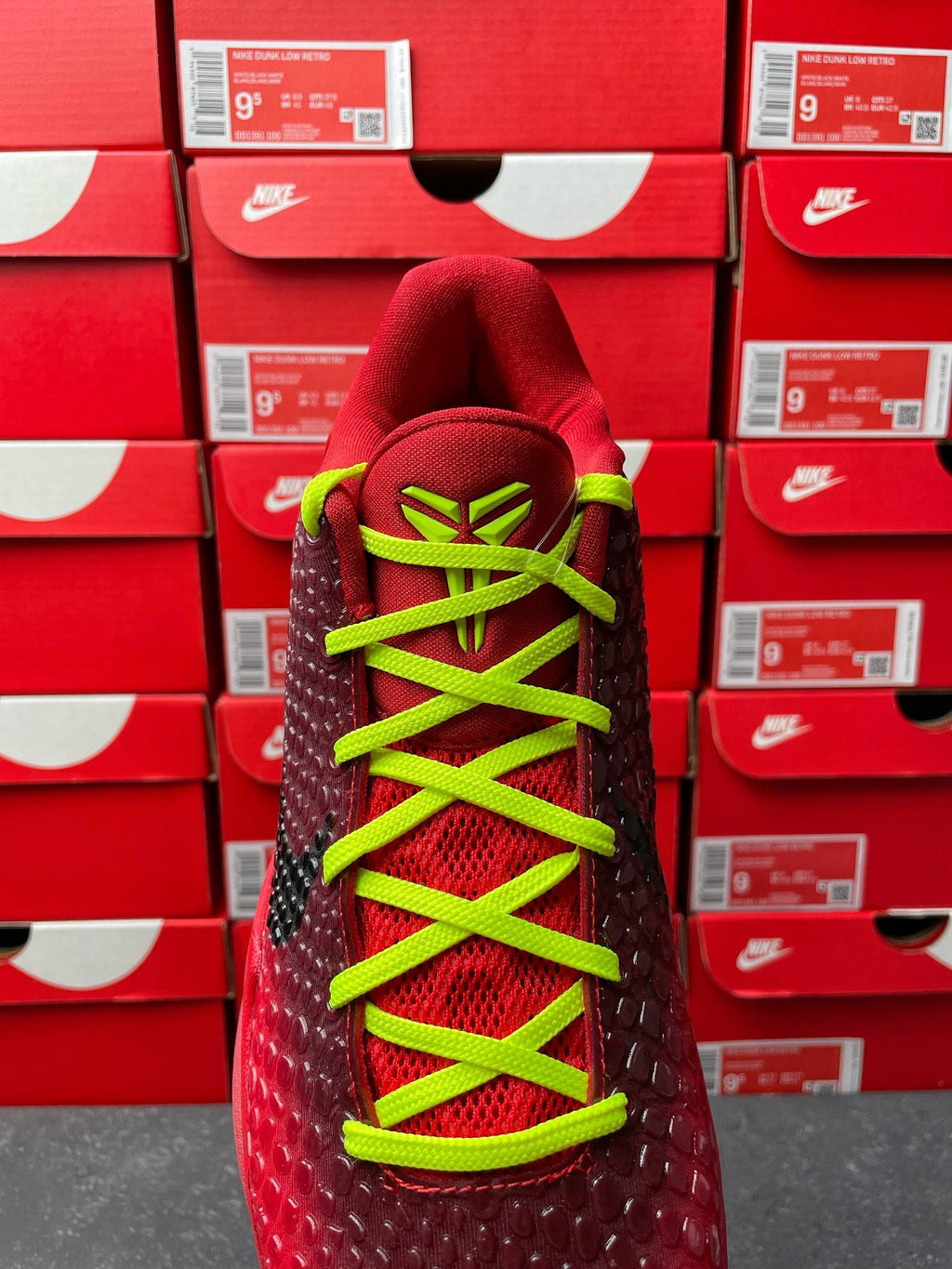 Red sneaker with neon green laces and black textured forefoot, front lace view.