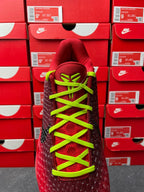 Red sneaker with neon green laces and black textured forefoot, front lace view.