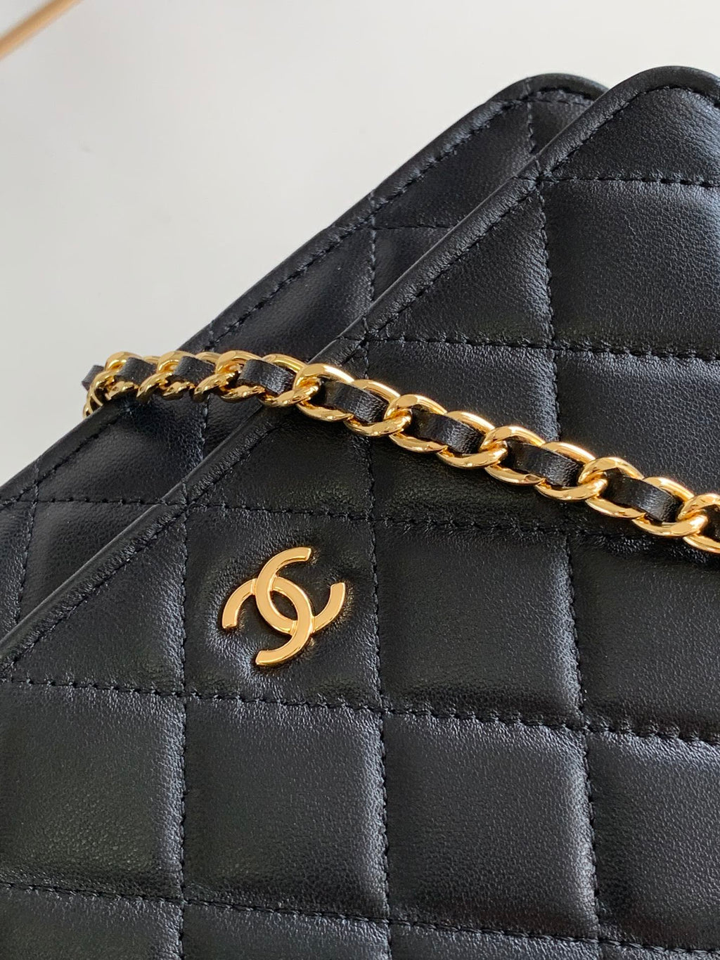 Close-up of quilted black leather bag flap with gold-tone chain and logo emblem