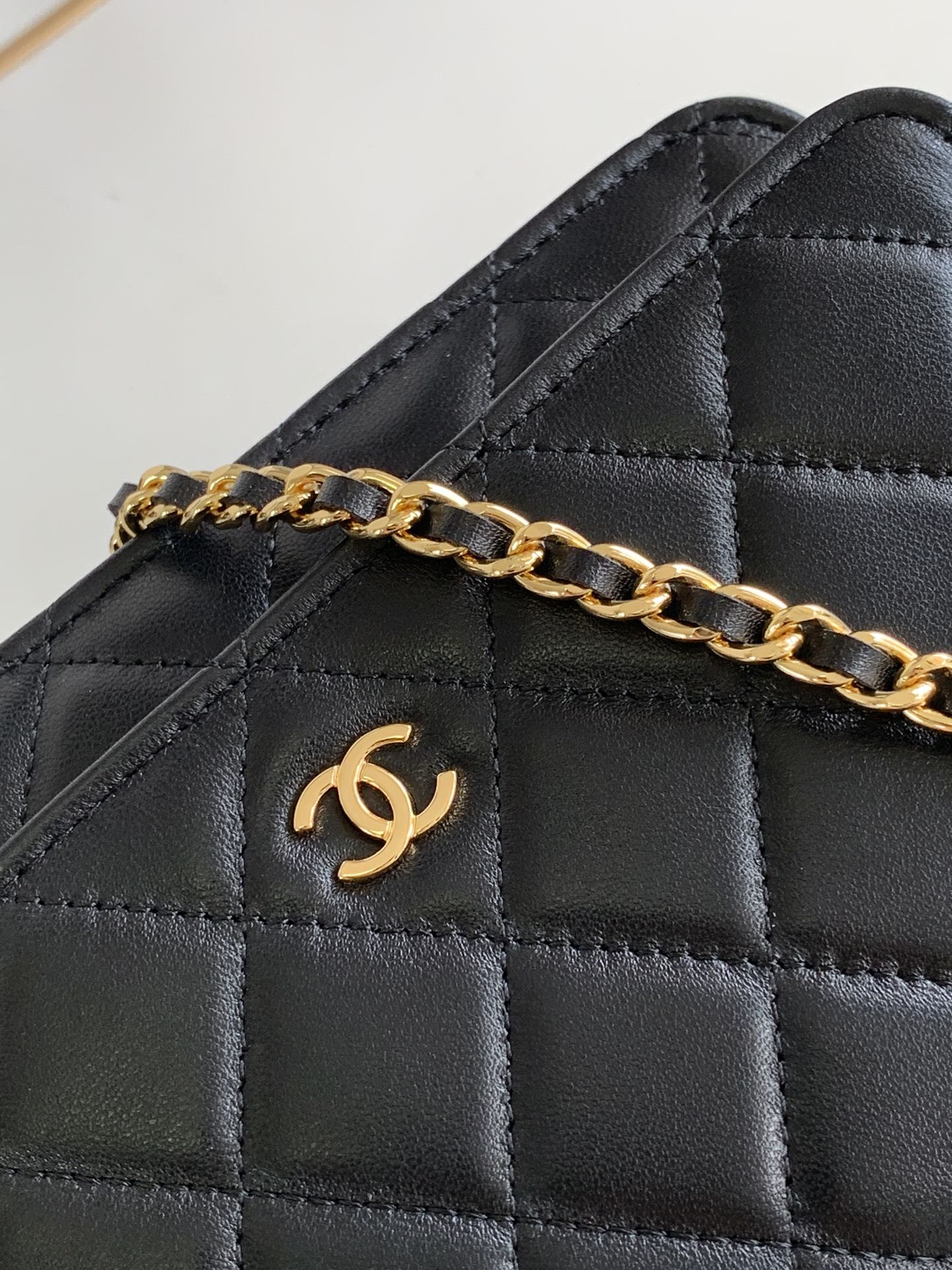 Close-up of quilted black leather bag flap with gold-tone chain and logo emblem