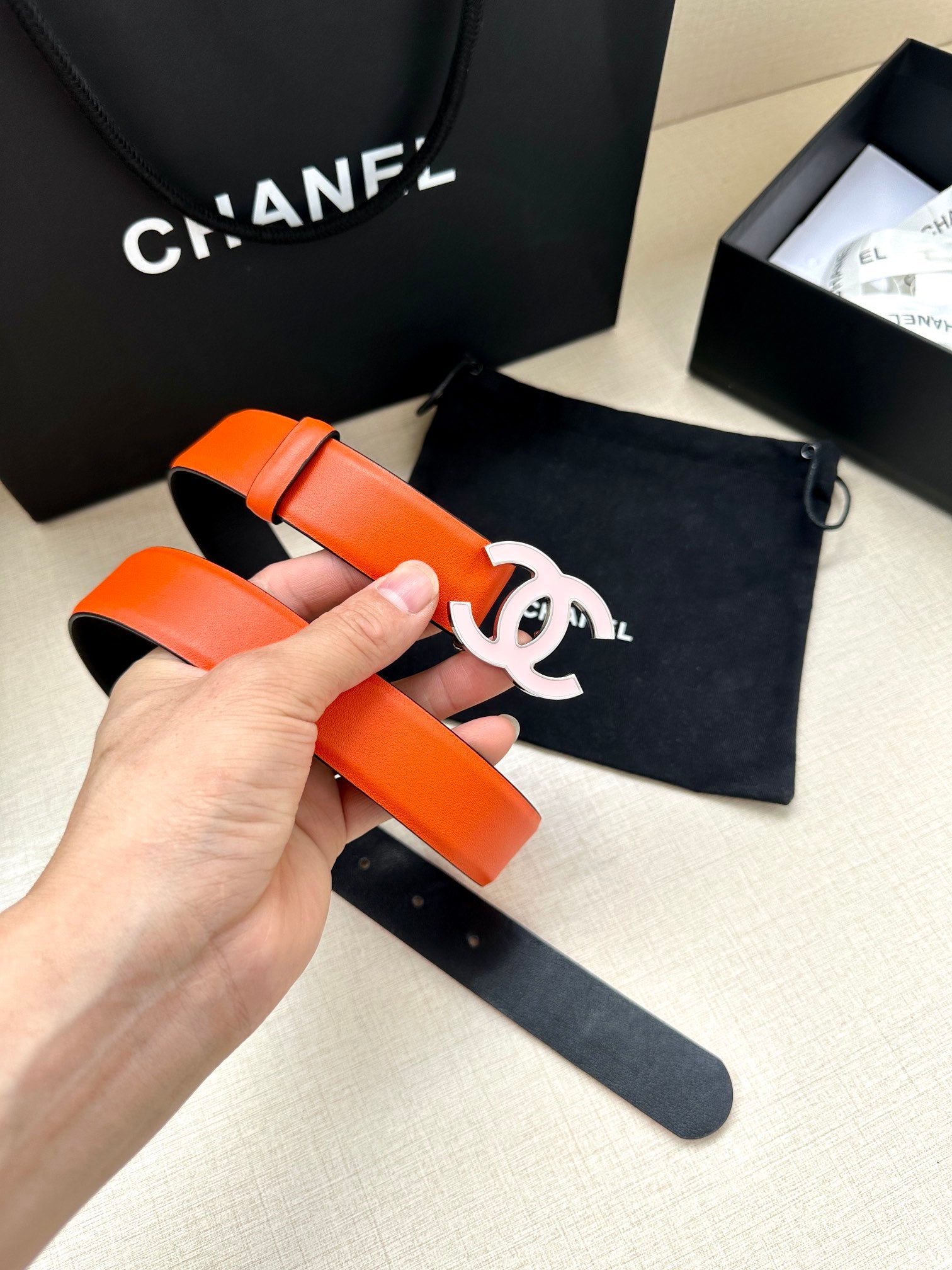 Orange Chanel belt held in hand, silver-tone CC buckle and strap holes