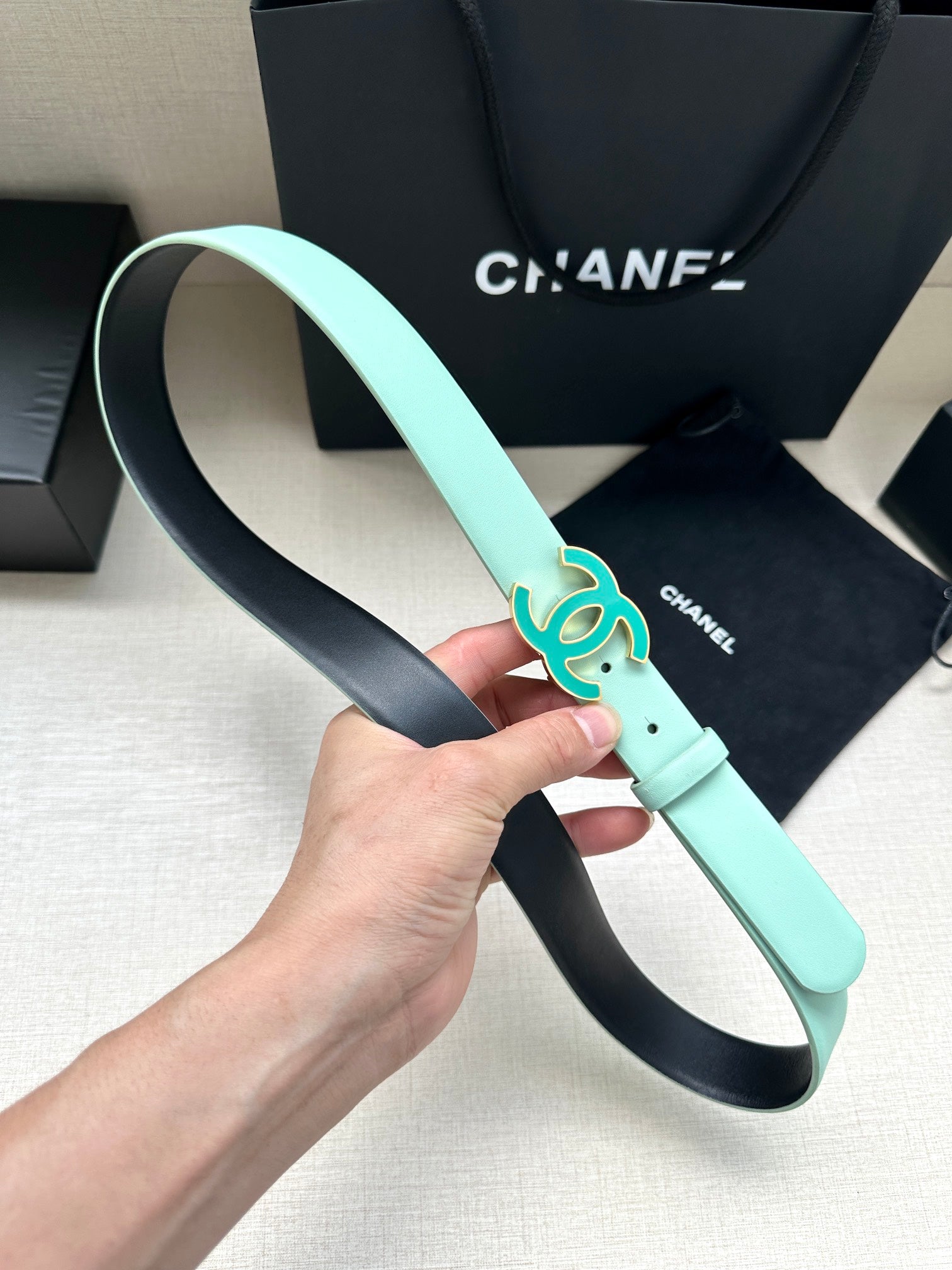 Mint Chanel belt held up, showing turquoise CC buckle and leather strap with holes.