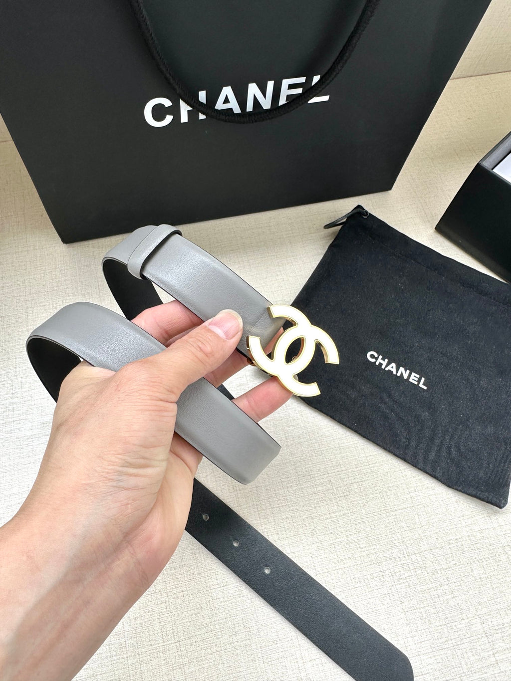 Gray leather belt with gold-tone CC logo buckle, close-up held in hand