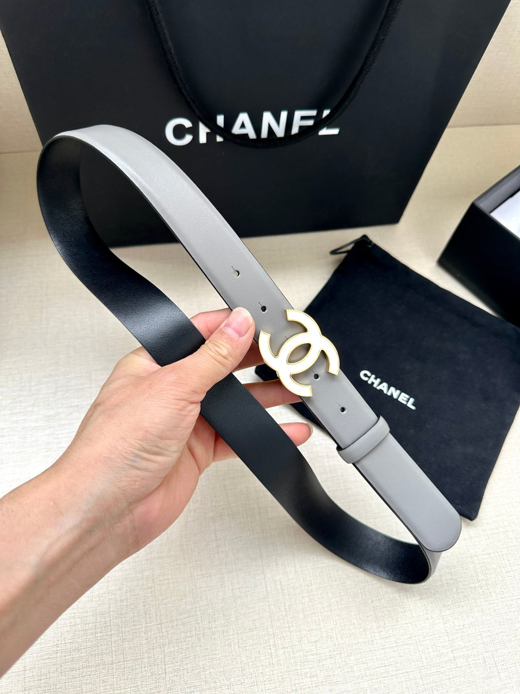 Gray leather Chanel belt with gold-tone CC logo buckle and end strap showing holes
