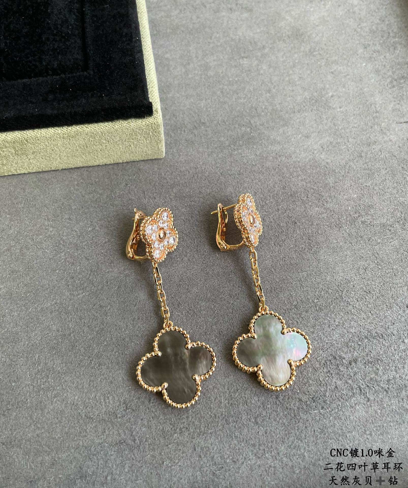 Gold clover drop earrings with dangling chain and pastel blue-green pendant on gray base
