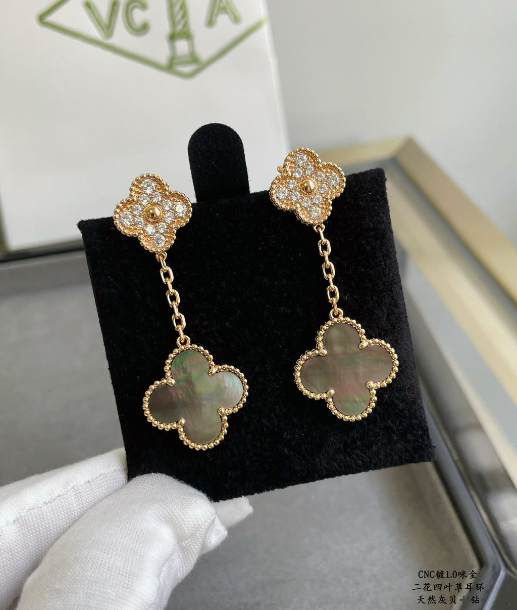 Gold clover drop earrings on black display with sparkling studs and light blue centers