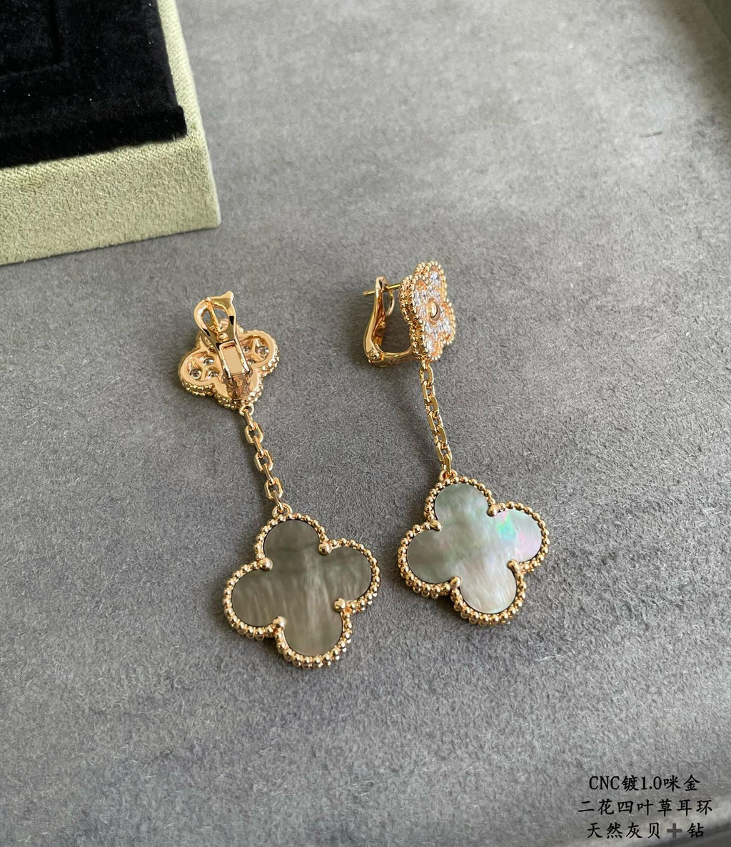 Gold clover drop earrings with dangling chain and pastel blue-green pendant on gray background