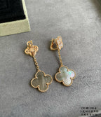 Gold clover drop earrings with dangling chain and pastel blue-green pendant on gray background