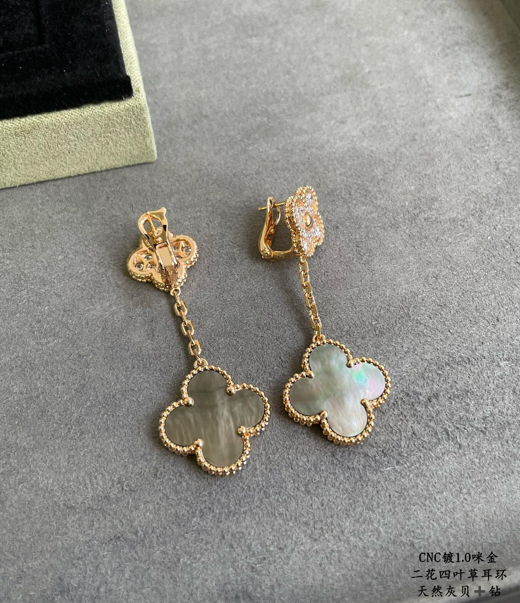 Gold clover drop earrings with dangling chain and pastel blue-green pendant on gray background