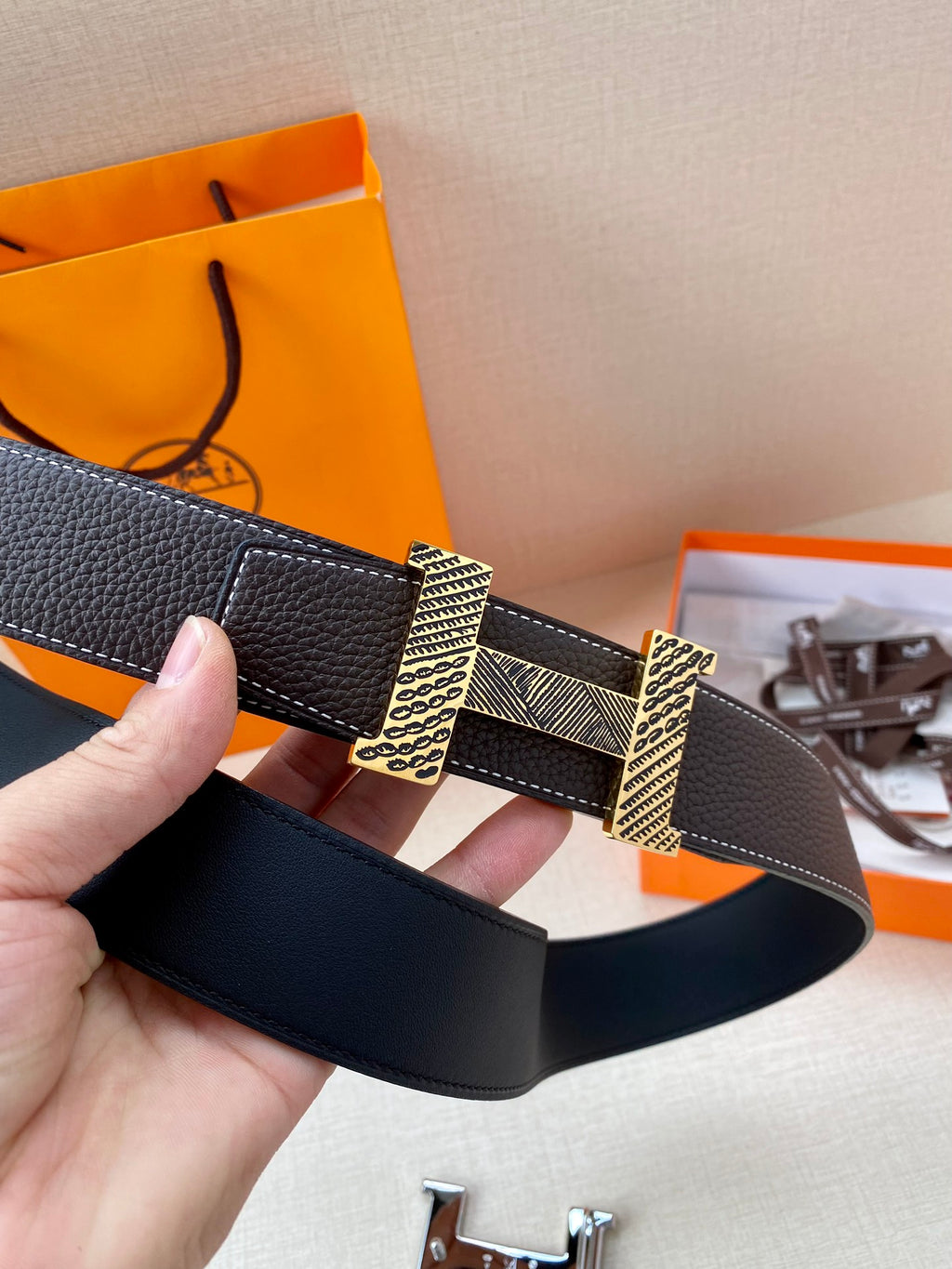 Hermes belt, dark leather, showing metal H buckle and patterned clasp segments.