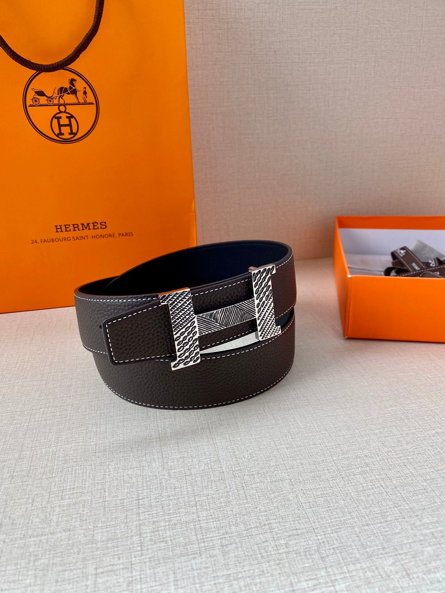 Hermes belt with dark leather body and metal H buckle with textured detail.