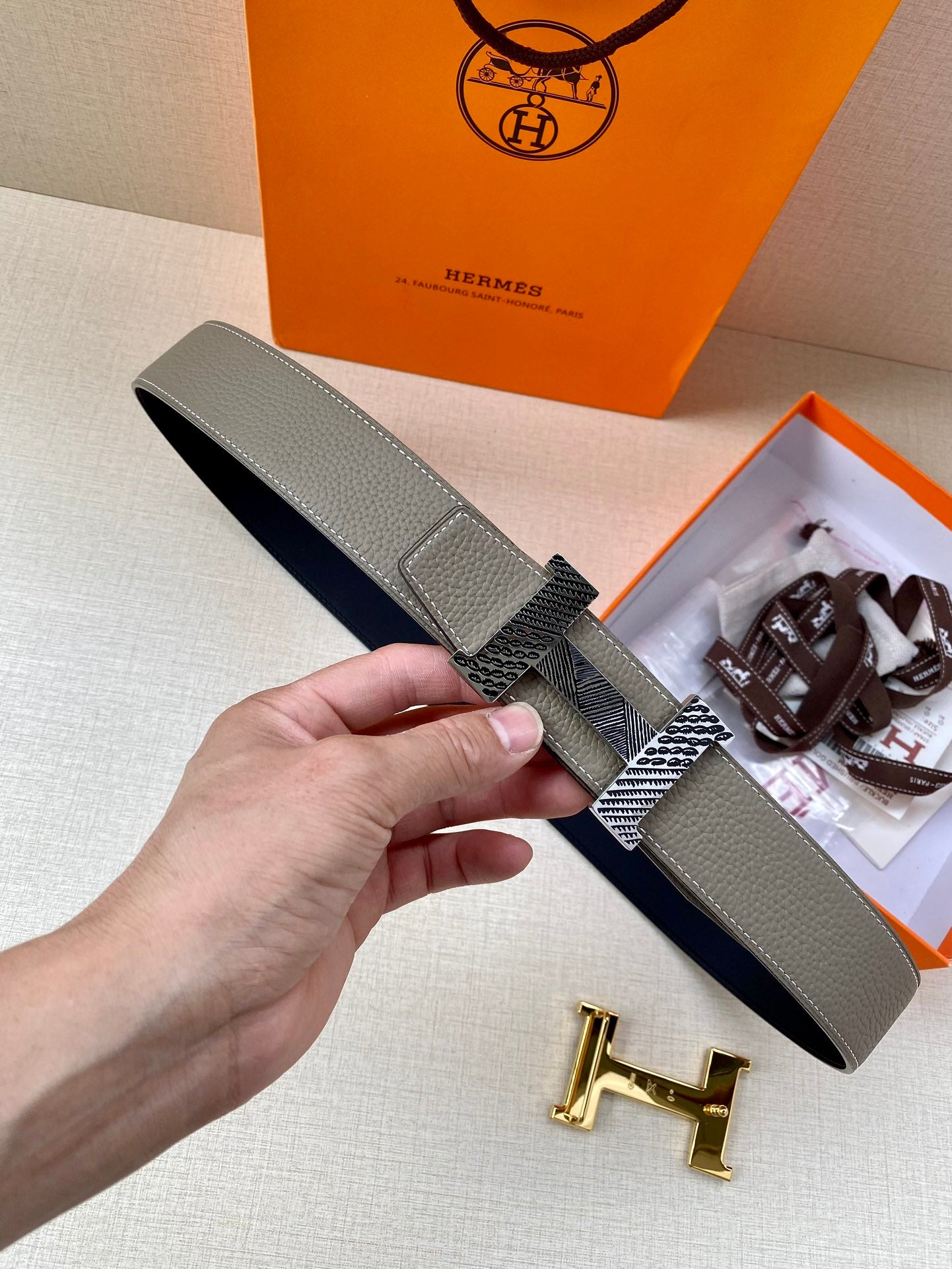 Two-tone leather belt with textured buckle strap, held in hand; gold-tone clasp detail