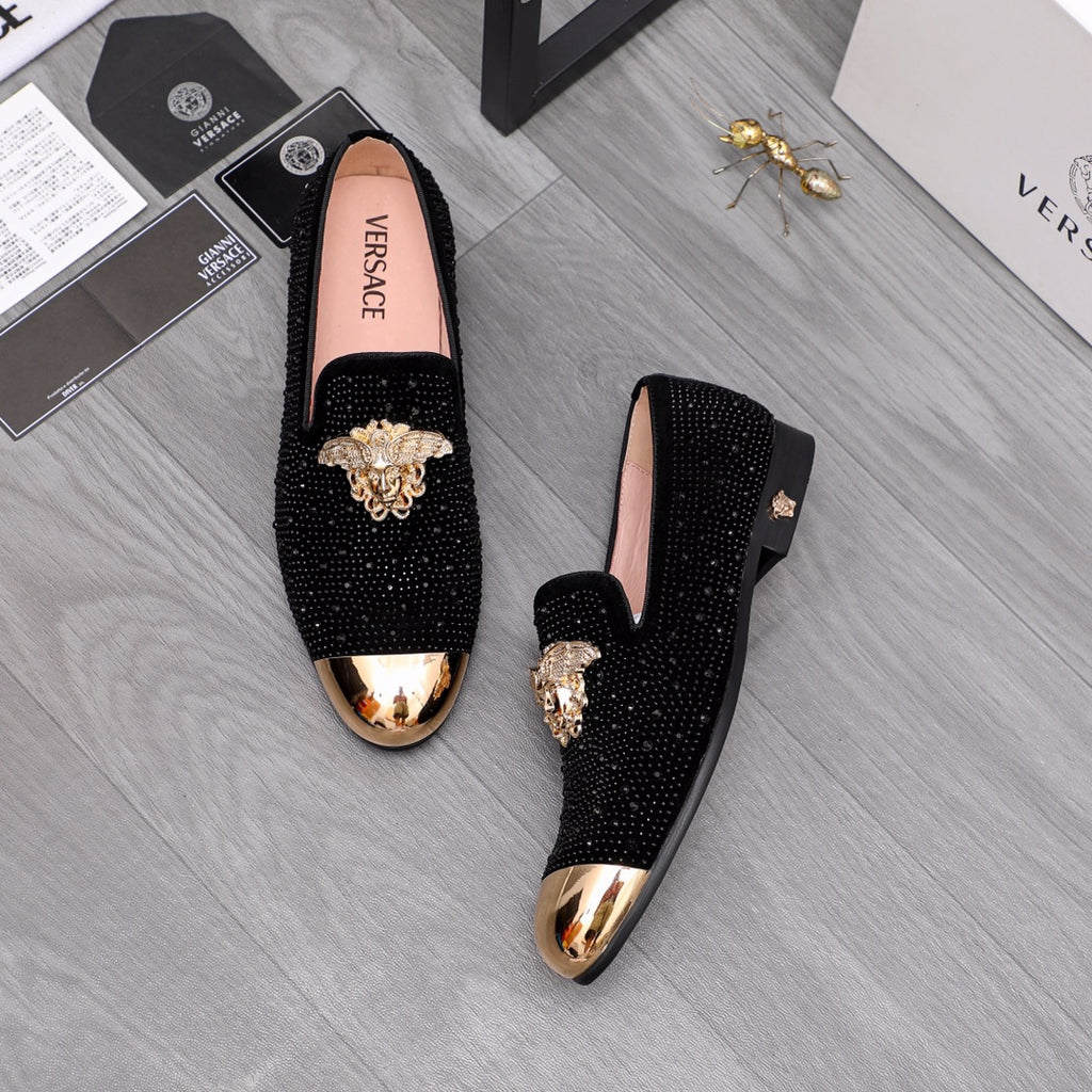 Black glitter loafers with gold-toned crest ornament, shown pair on the floor