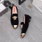 Black glitter loafers with gold-toned crest ornament, shown pair on the floor