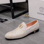 White studded slip-on loafer with gold medallion and low dark sole, side view