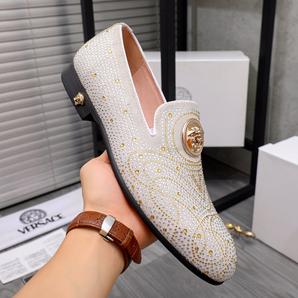 White studded slip-on loafer with gold medallion detail and low dark sole, angled close-up