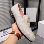 White studded slip-on loafer with gold medallion detail and low dark sole, angled close-up