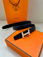 Dark blue leather belt with large silver H buckle laid on orange box
