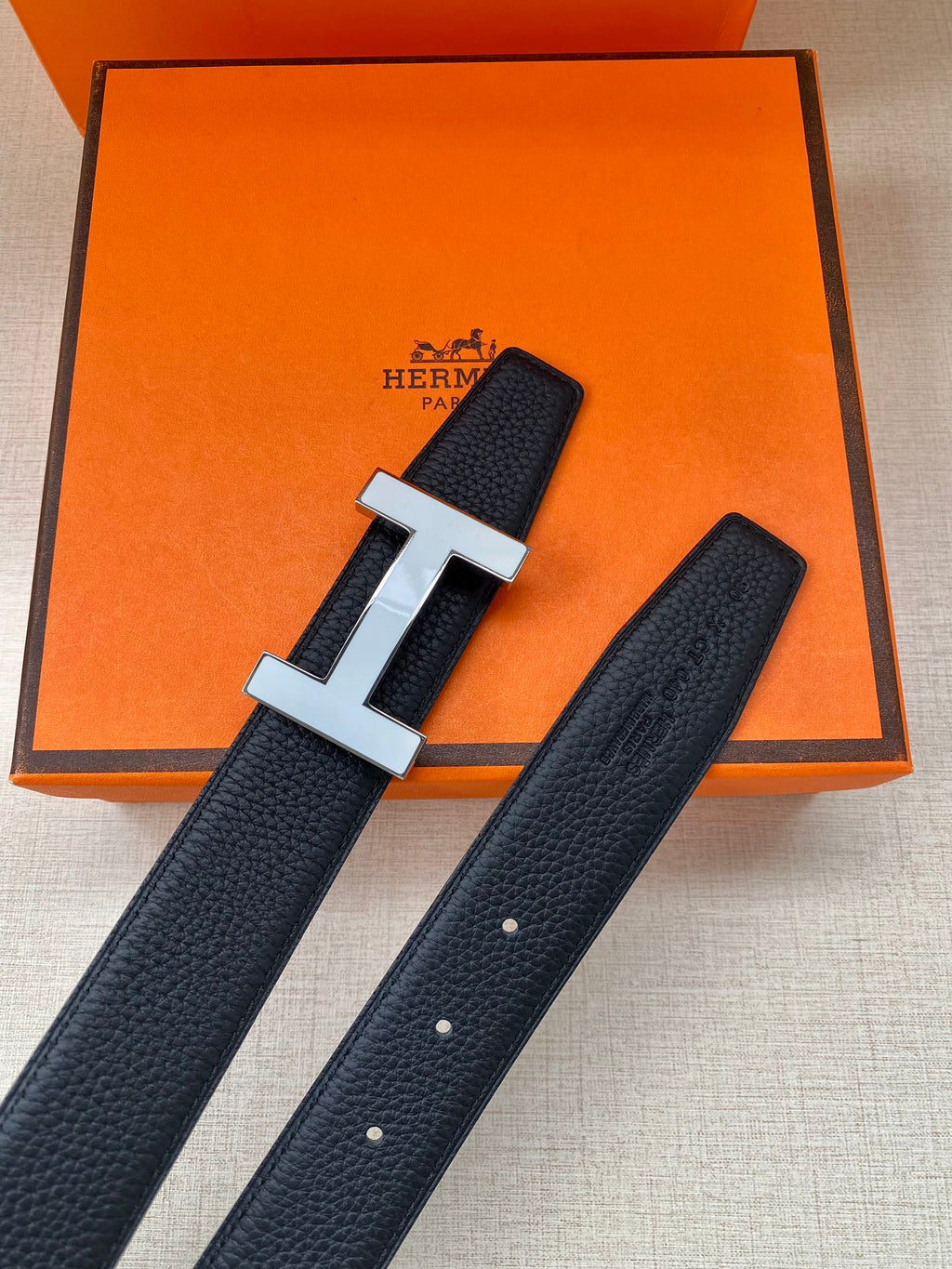 Dark blue leather belt with silver H buckle on orange display box