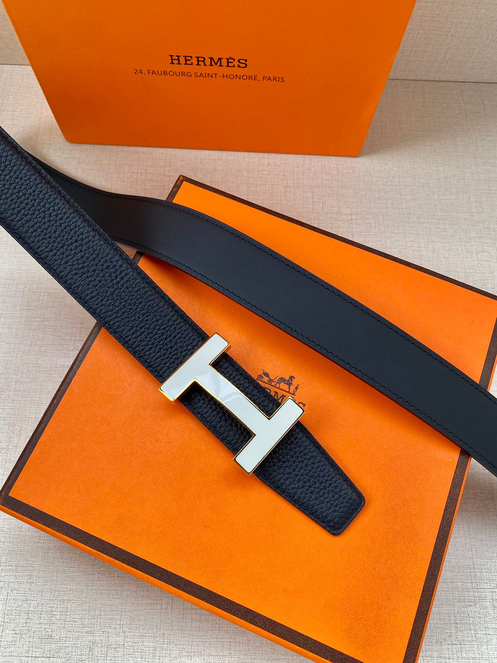 Dark blue leather belt with silver H buckle resting on orange packaging