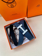 Blue leather belt with silver H buckle, coiled inside an orange box.