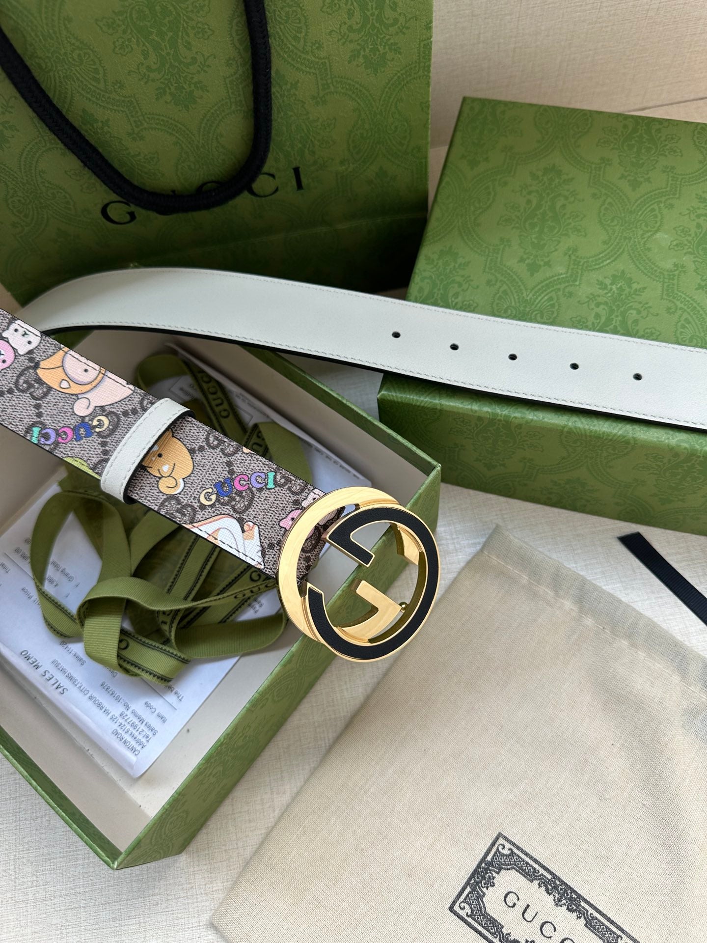 Gucci belt in packaging with cartoon print strap and gold-toned round logo buckle