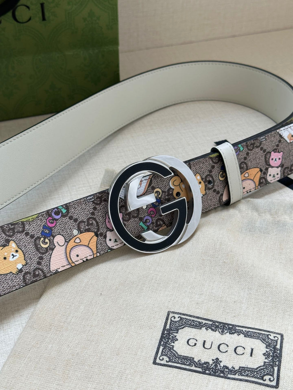 Gucci belt showing round buckle detail and multicolor cartoon pattern on light gray leather