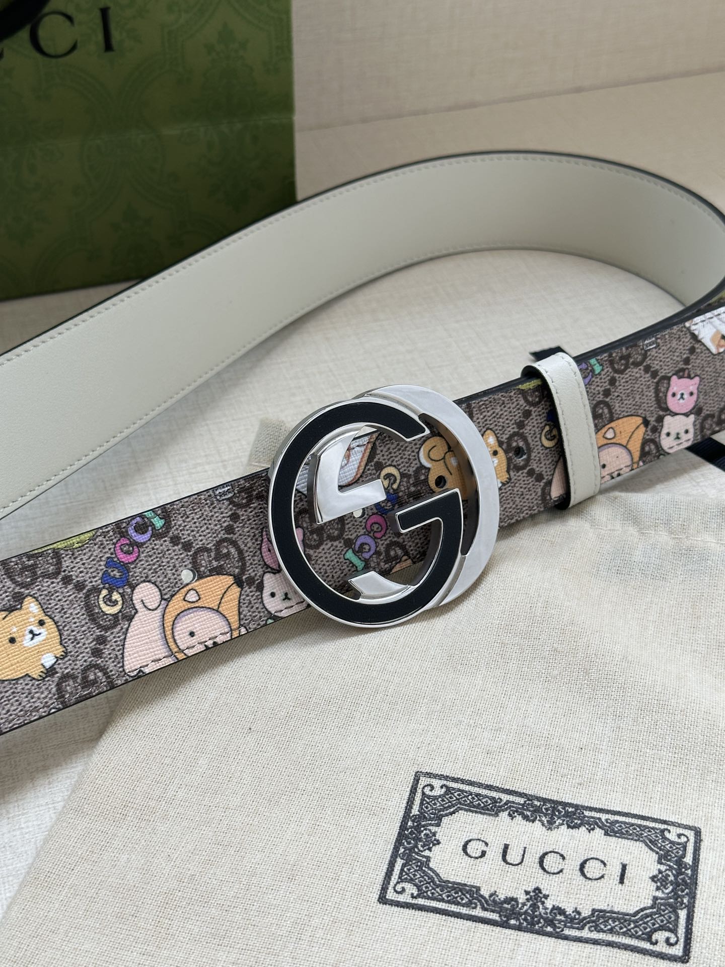 Gucci belt showing round buckle detail and multicolor cartoon pattern on light gray leather