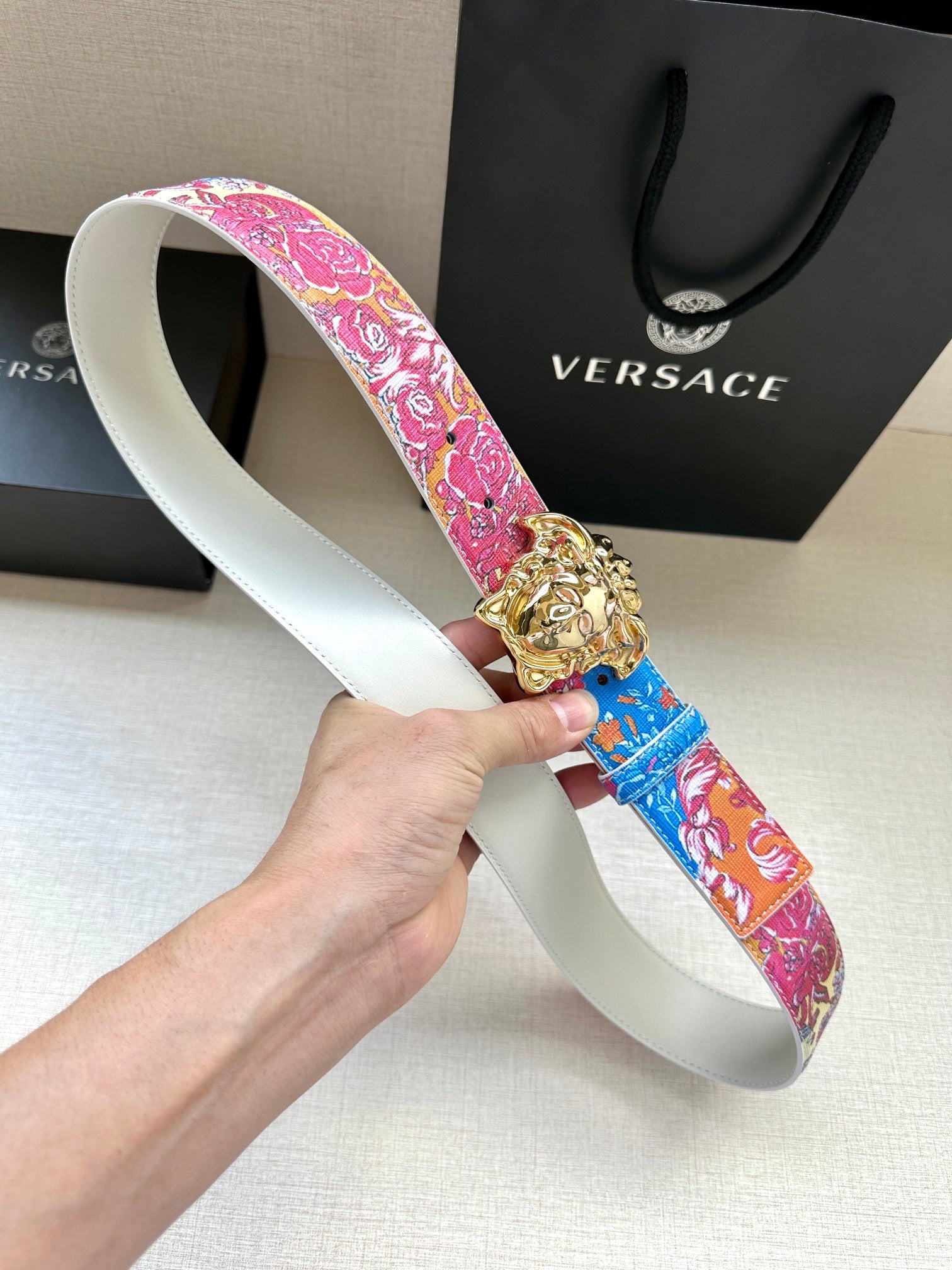 Versace belt with pink and blue floral strap and gold lion buckle on white