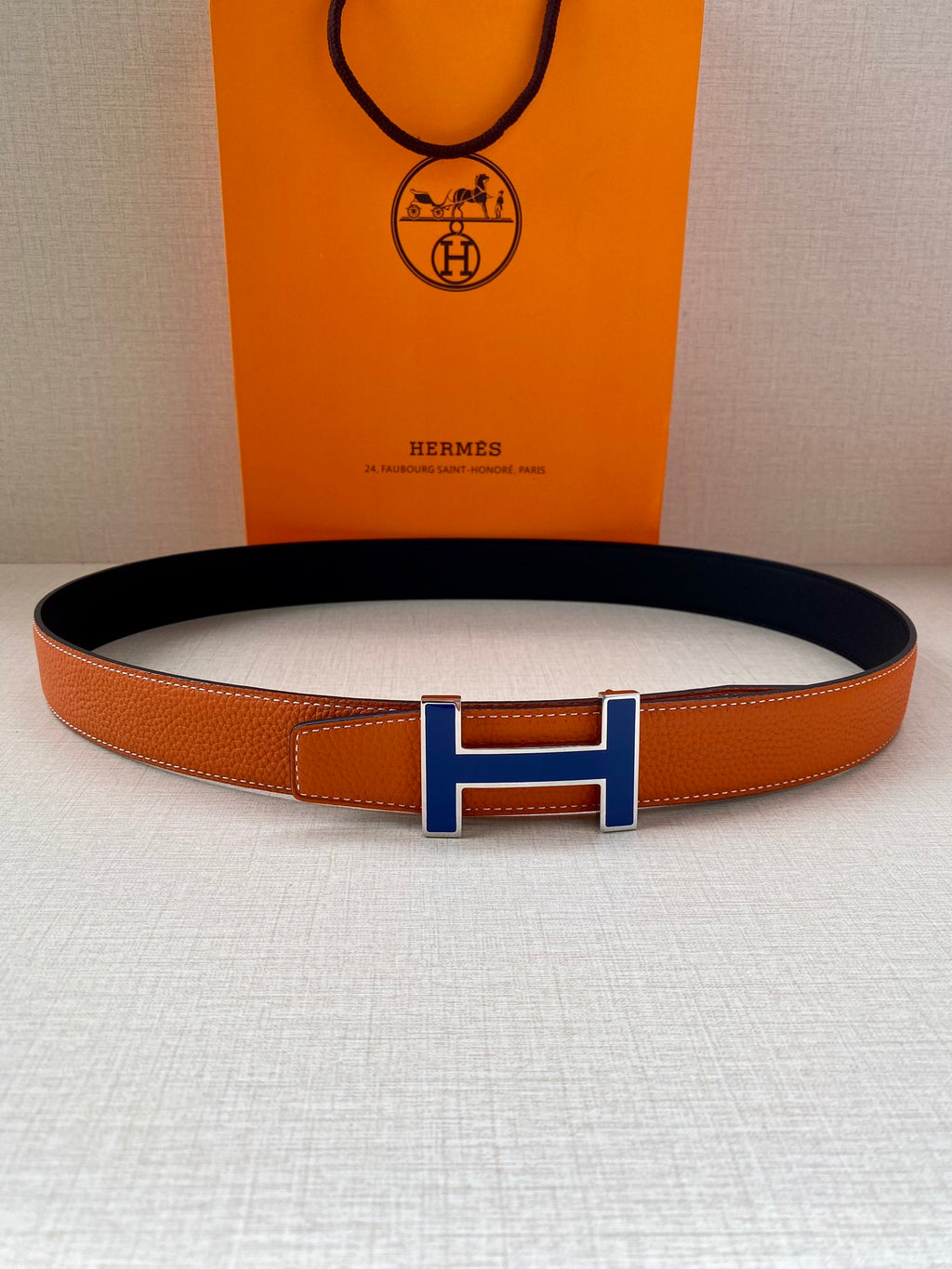 Hermes belt with orange leather strap and blue H buckle, laid flat