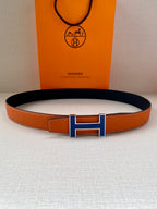 Hermes belt with orange leather strap and blue H buckle, laid flat