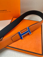Hermes belt detail with blue H buckle on orange leather strap
