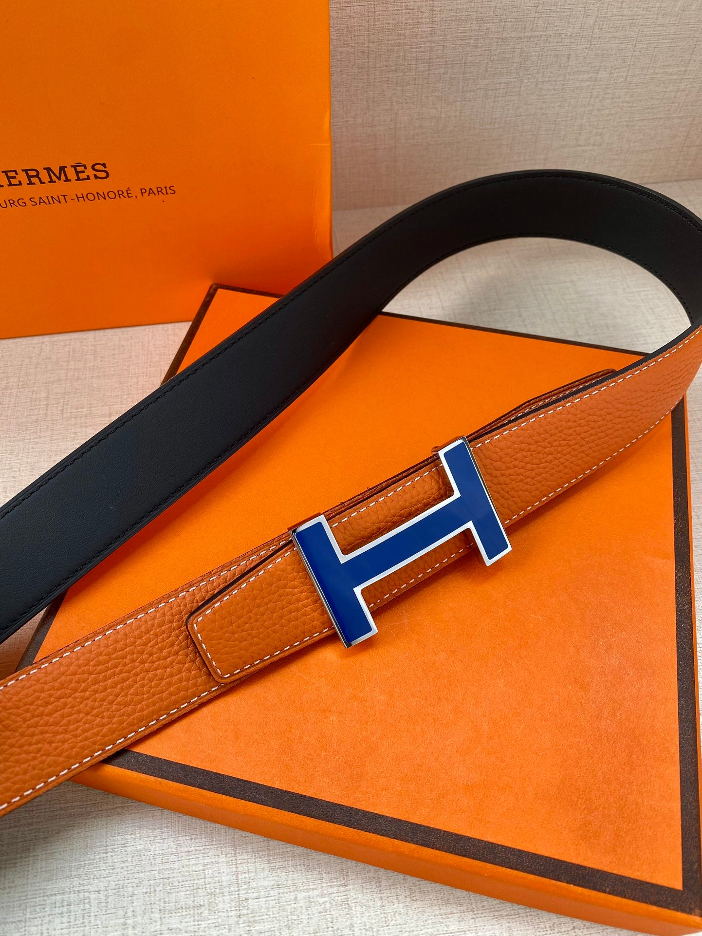 Hermes belt detail with blue H buckle on orange leather strap