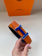 Hermes belt with orange leather strap and blue H buckle, rolled end view