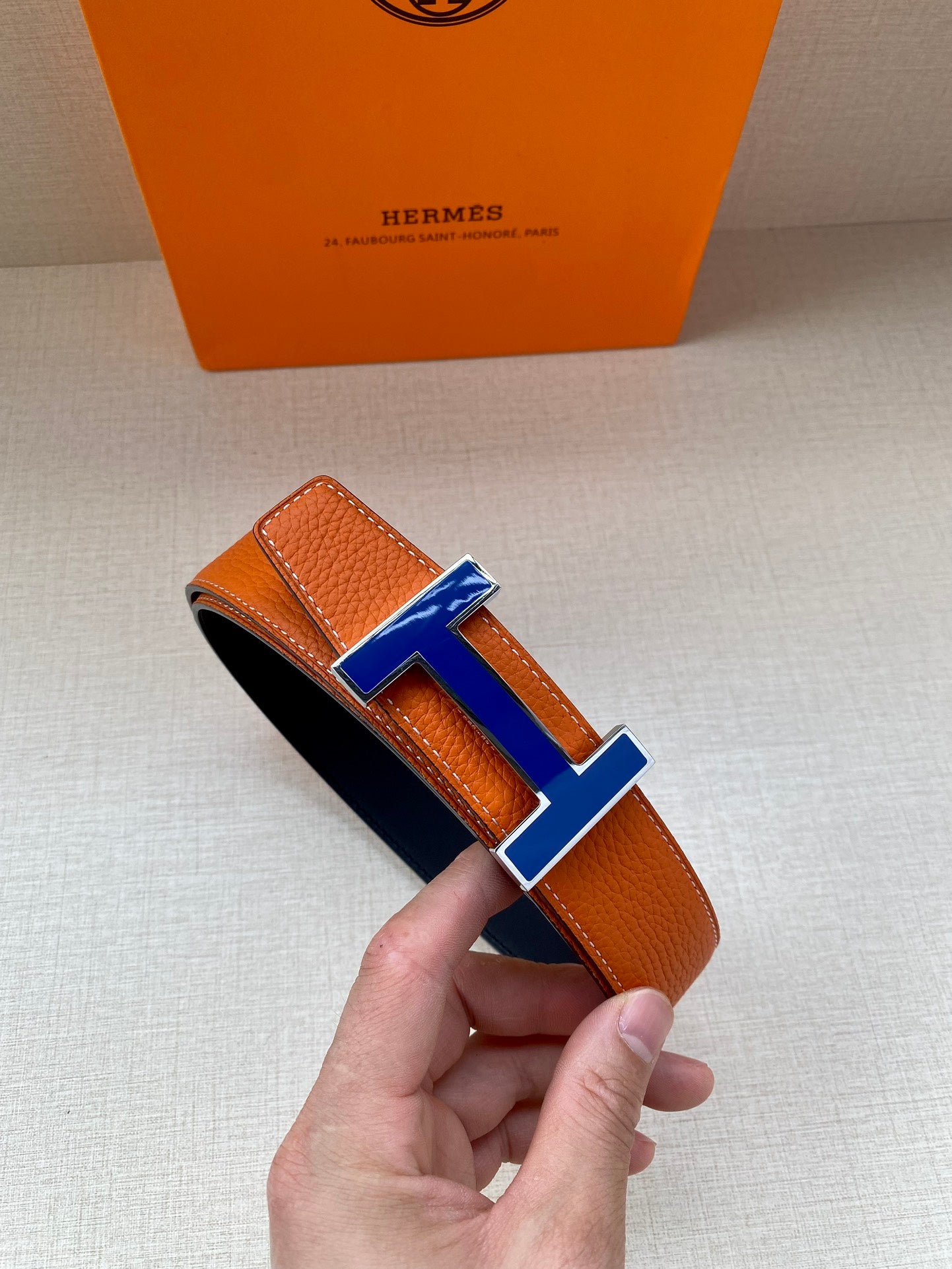 Hermes belt with orange leather strap and blue H buckle, rolled end view