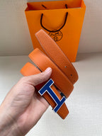 Hermes belt with orange leather strap and blue H buckle, shown close-up