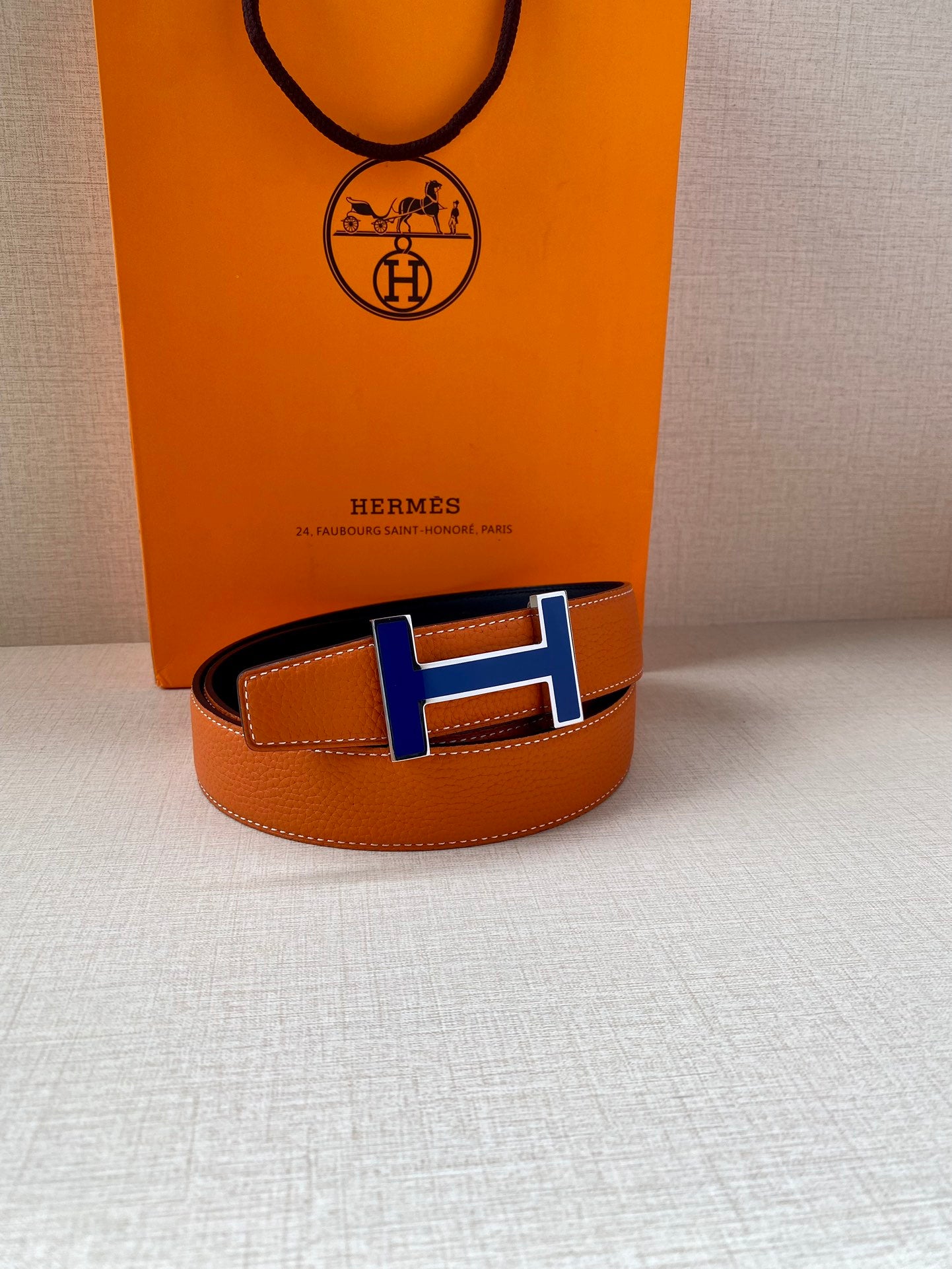 Hermes belt with orange strap, dark leather edge, and blue H buckle