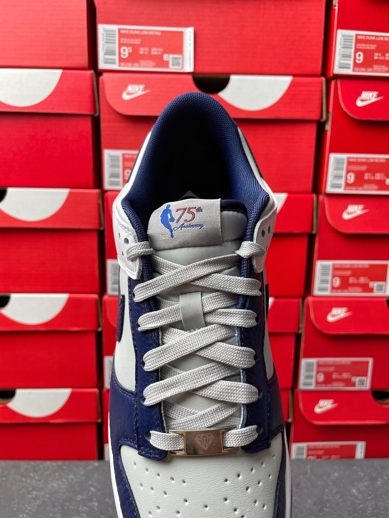 Low-top sneakers, white tongue patch with blue graphic, gray eyelets, lace-up design.