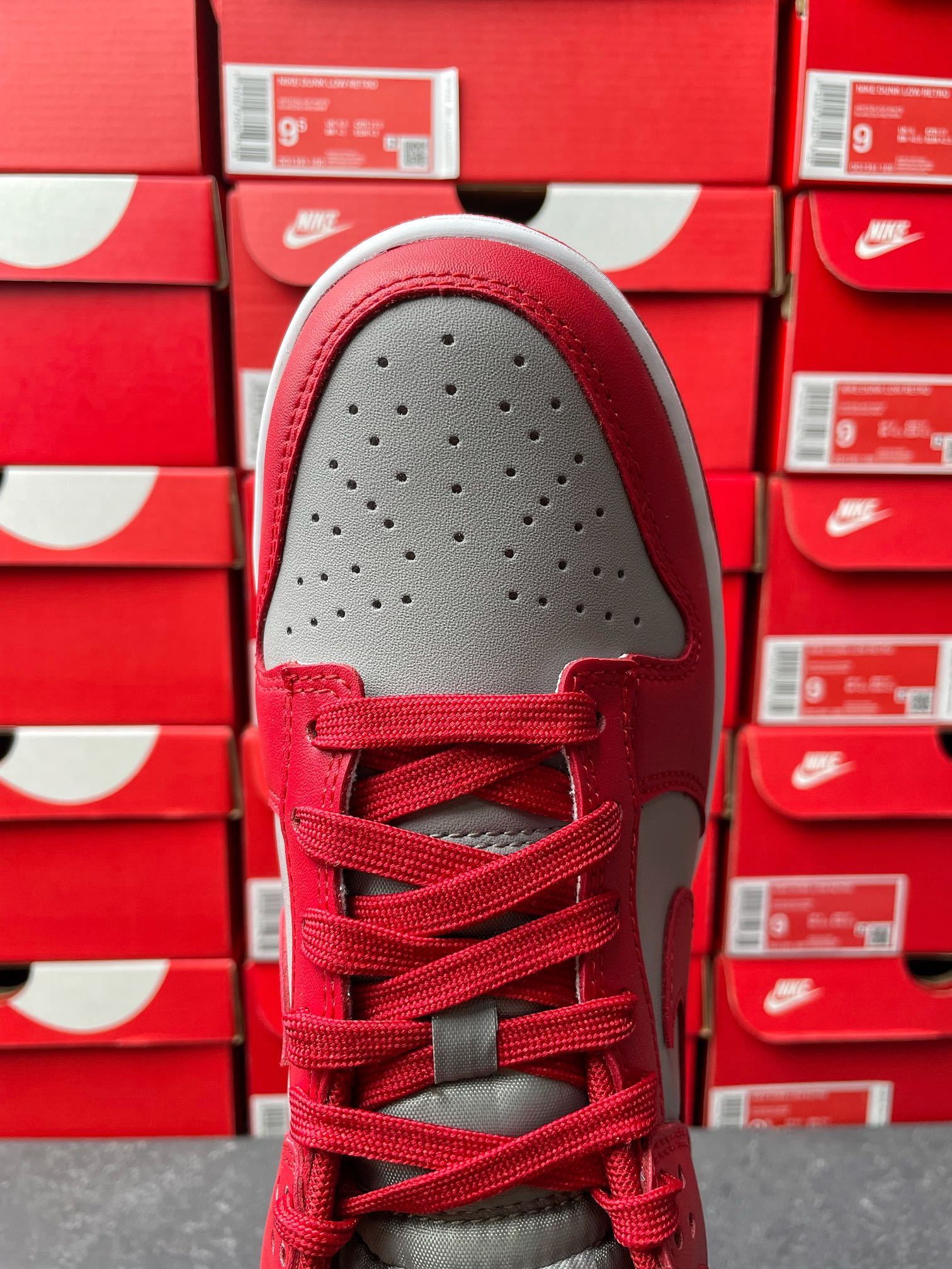 Low-top sneaker toe view with red upper, gray toe cap, perforations, and red laces.