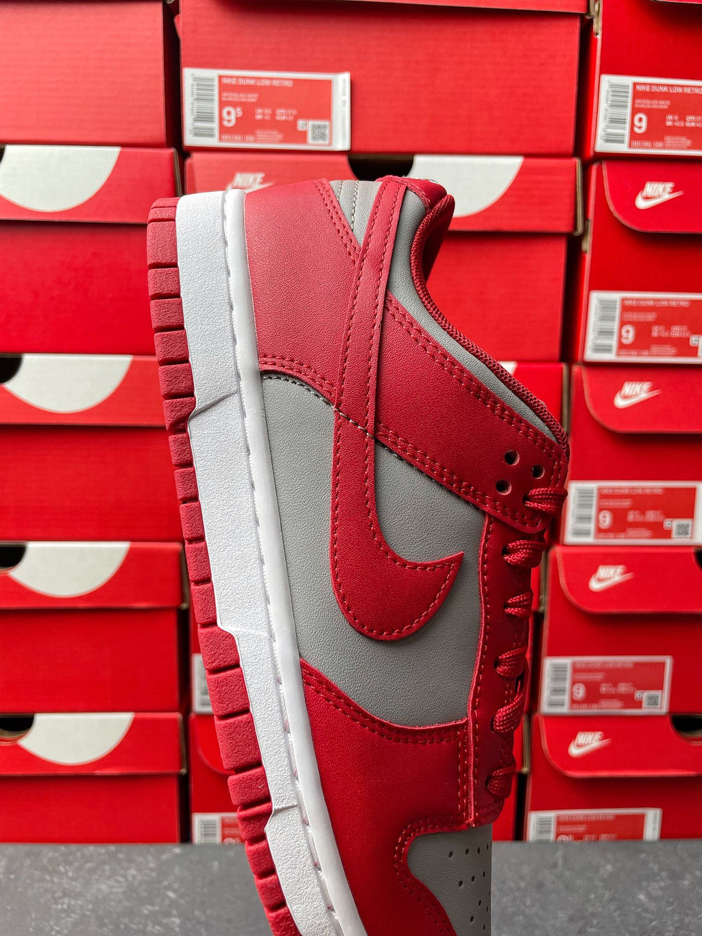 Low-top sneaker with red upper, gray overlays, red lace-up, and white midsole.