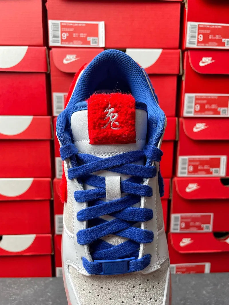Nike Dunk Low sneakers with blue laces, light gray suede, and red accent tongue.