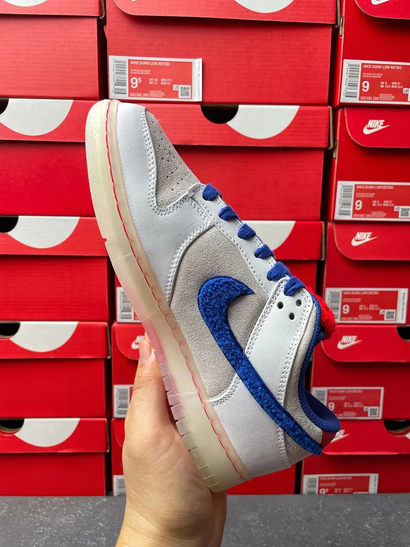 Nike Dunk Low sneakers angled side view, light gray leather with blue swoosh and red lining.