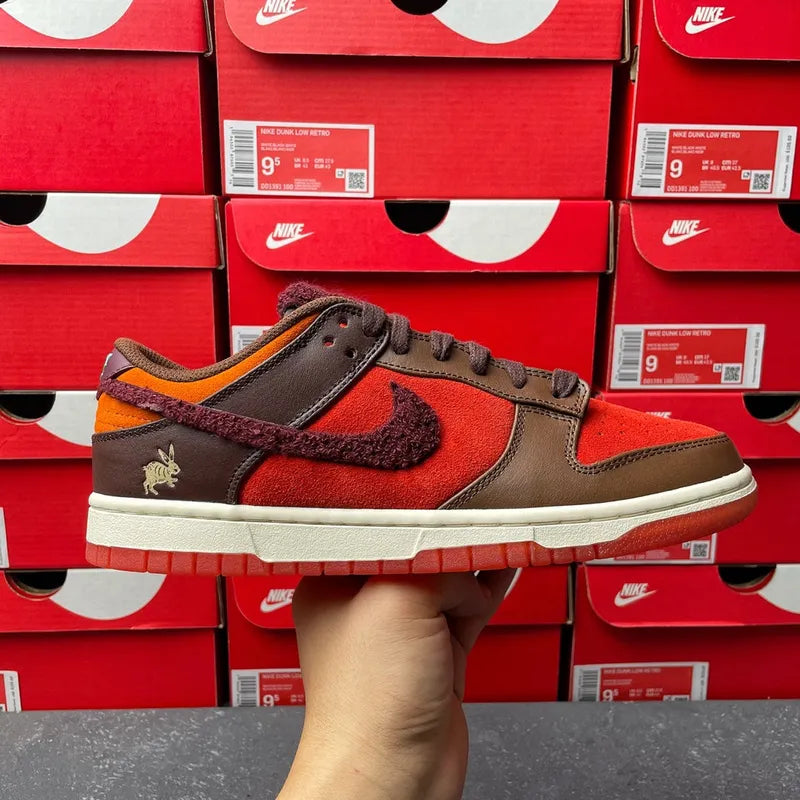 Nike Dunk Low sneakers with red suede, brown leather, and dark swoosh detail.