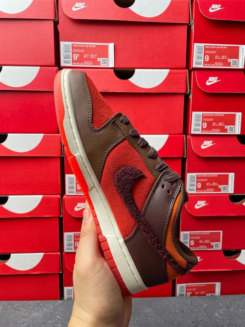 Nike Dunk Low sneaker angled side view with red suede panels and brown overlays.