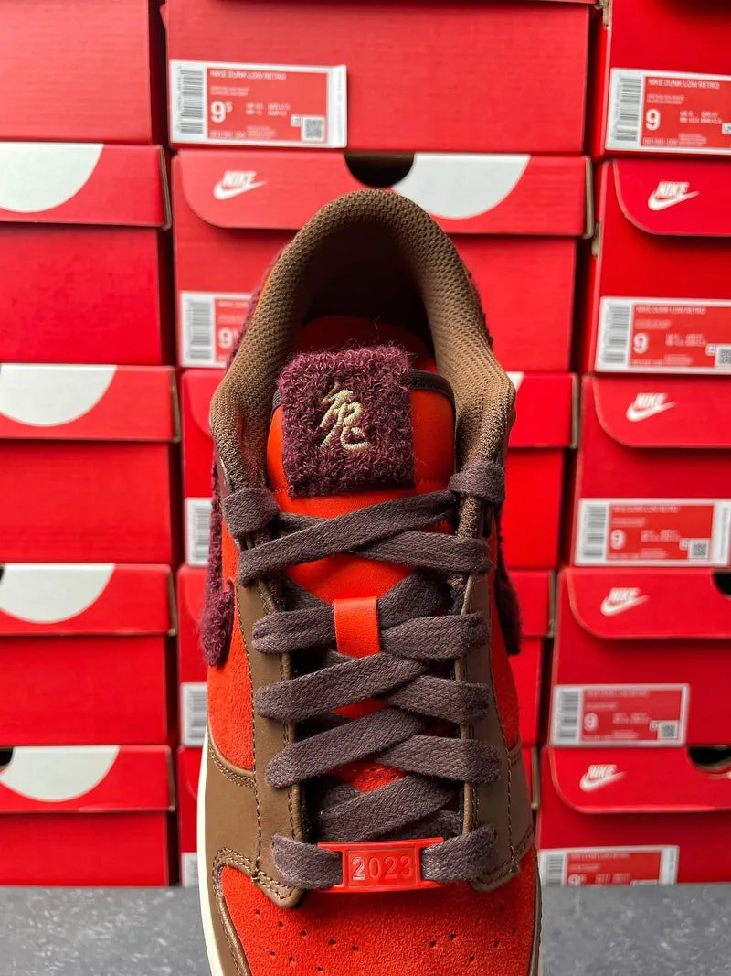 Nike Dunk Low sneaker lace and tongue view in brown suede and red-orange accents.