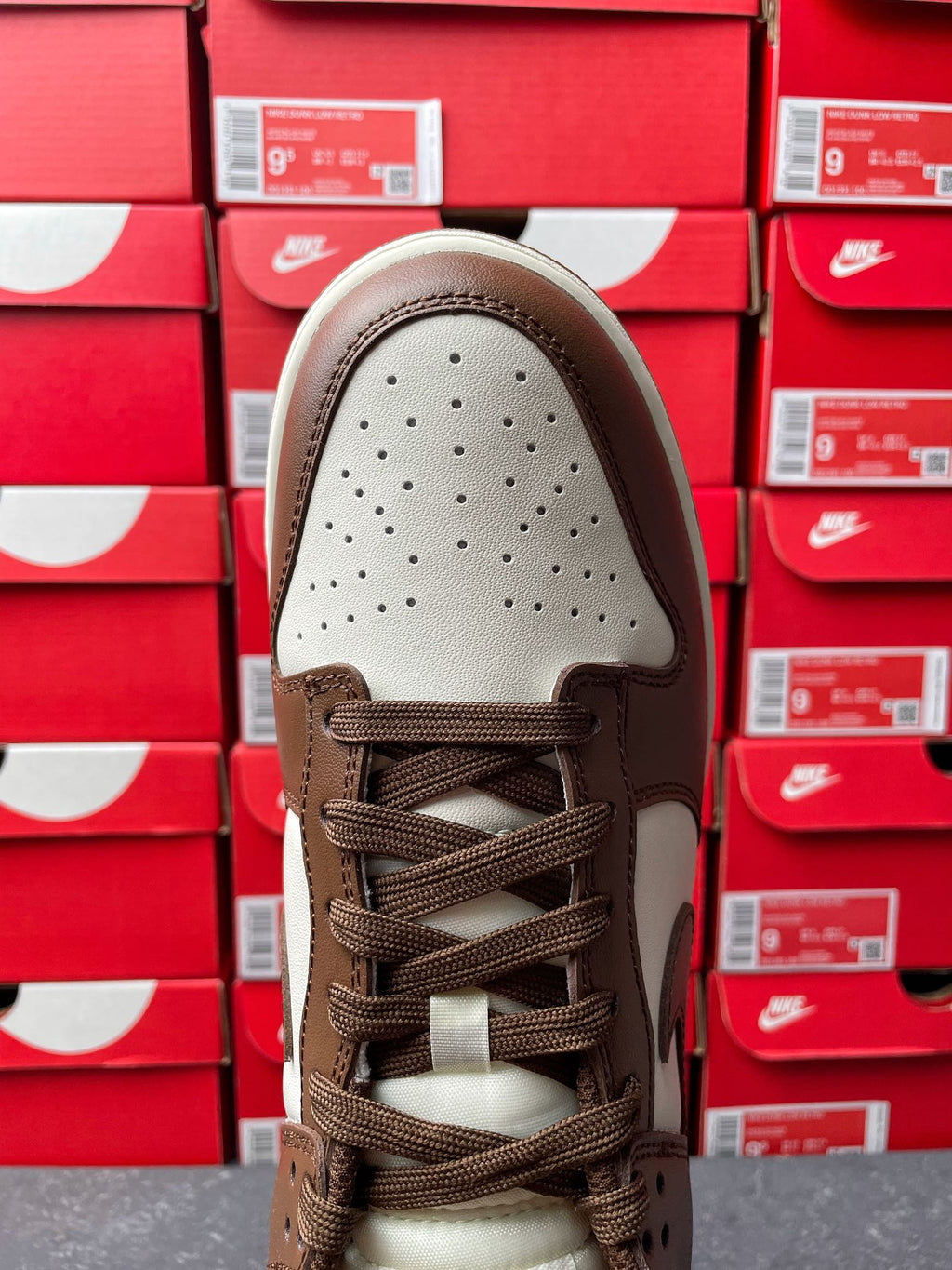 Low-top sneaker toe view with perforated white panel and brown lace-up