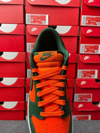Green low-top sneaker heel with orange laces and orange stripe, white midsole.