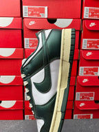 Nike Dunk Low sneaker quarter view in dark green, white panels, and cream sole