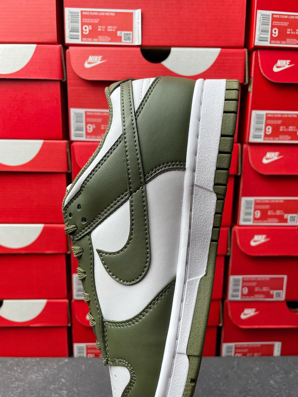 Low-top sneaker side view with olive green upper, white swoosh, and thick white sole.
