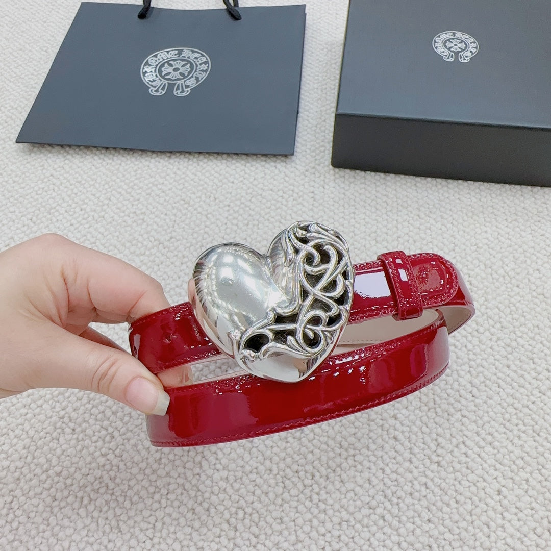 Red patent leather belt with silver heart buckle, side view in hand.
